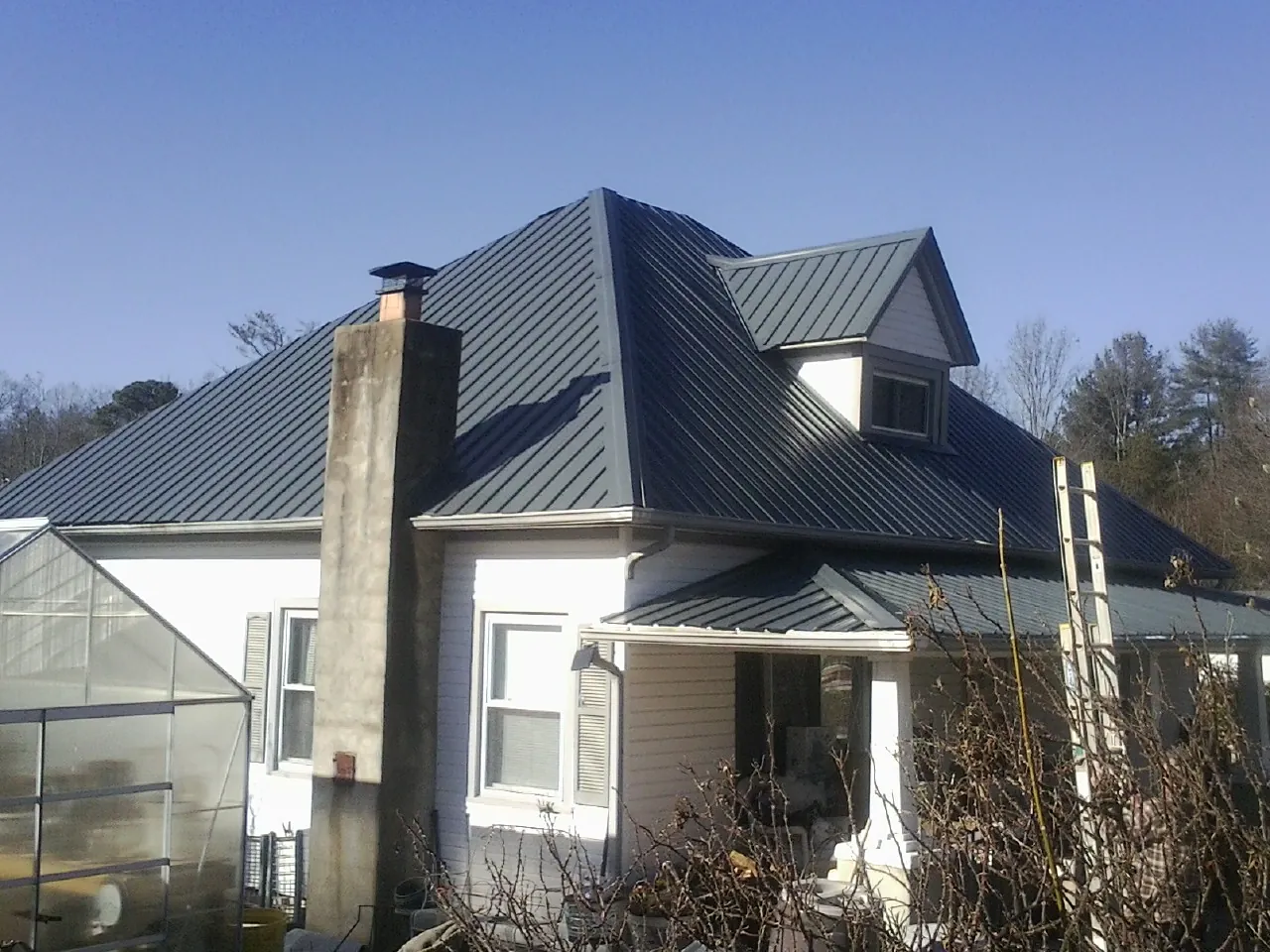 Dark blue standing seam metal roof on a white farmhouse with dormer — Slate & Tile Roof Repair by Roofing Brothers in West Des Moines