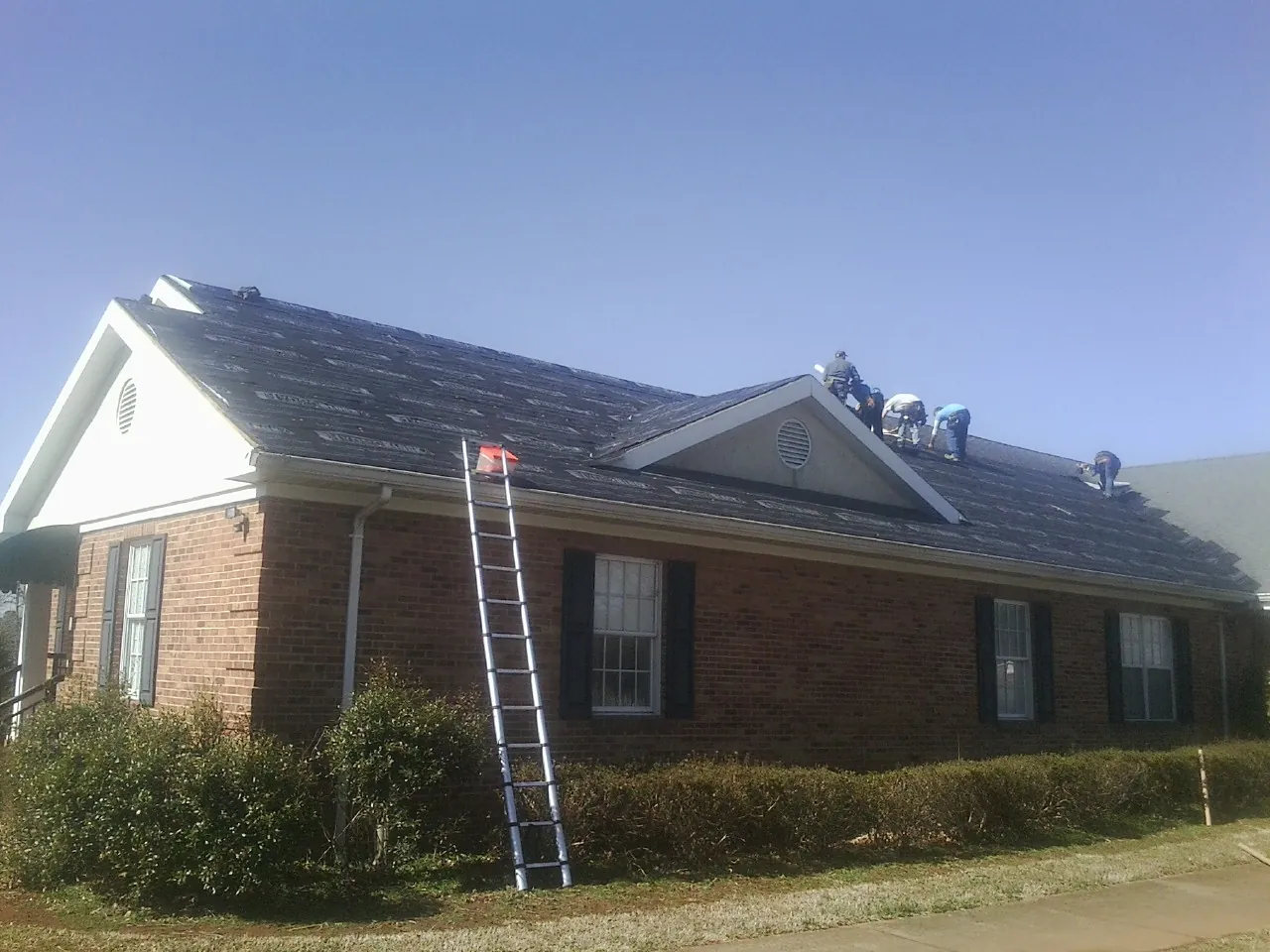 Crew tearing shingles off a brick ranch roof with a ladder set — Emergency Roof Repair work by our crew in West Des Moines