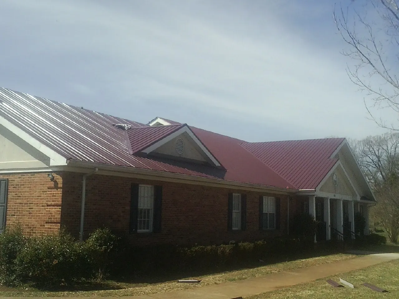 Red metal roof with gabled entries on a long brick building, from a Hail Damage Roof Repair job in West Des Moines