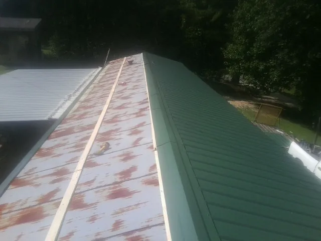 Old rusted panels beside newly installed green metal roofing — Wind Damage Roof Repair by Roofing Brothers in West Des Moines