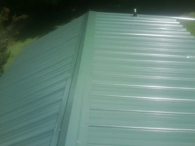 New green metal panels meeting at the ridge of a roof — Flat Roof Repair work by our crew in West Des Moines
