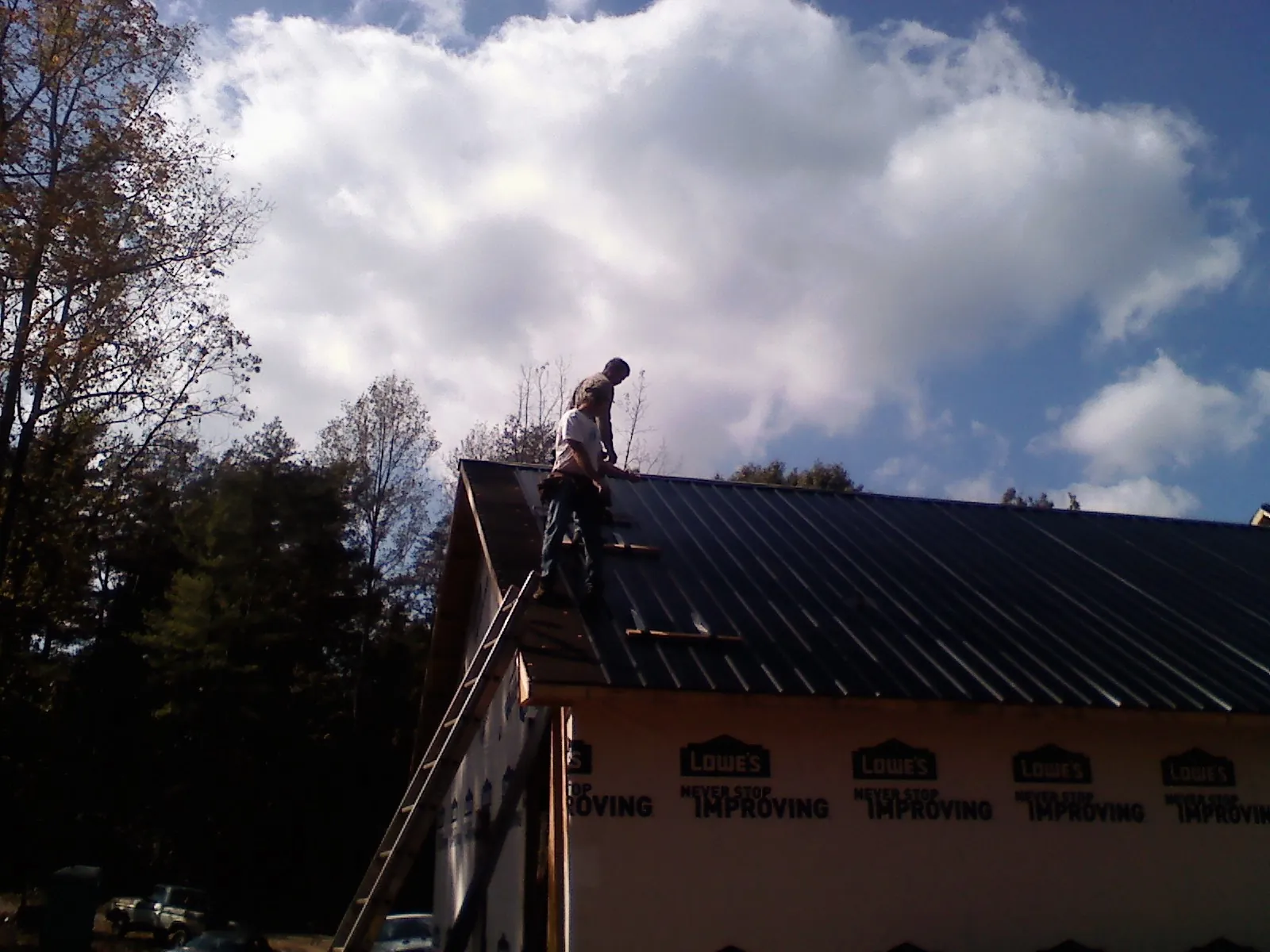Roofer fastening dark metal panels high against a cloudy sky, from a Roof Inspection job in West Des Moines