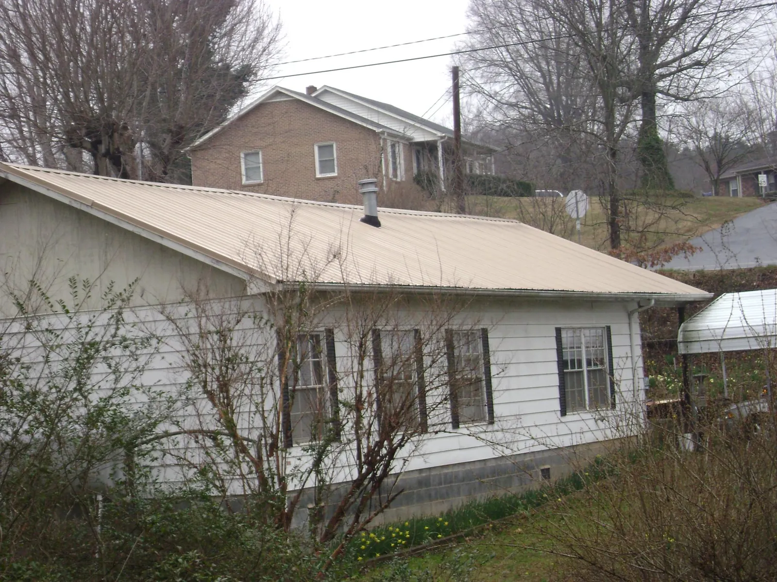 Tan metal roof on a white sided house set into a hillside — Commercial Roofing by Roofing Brothers in West Des Moines