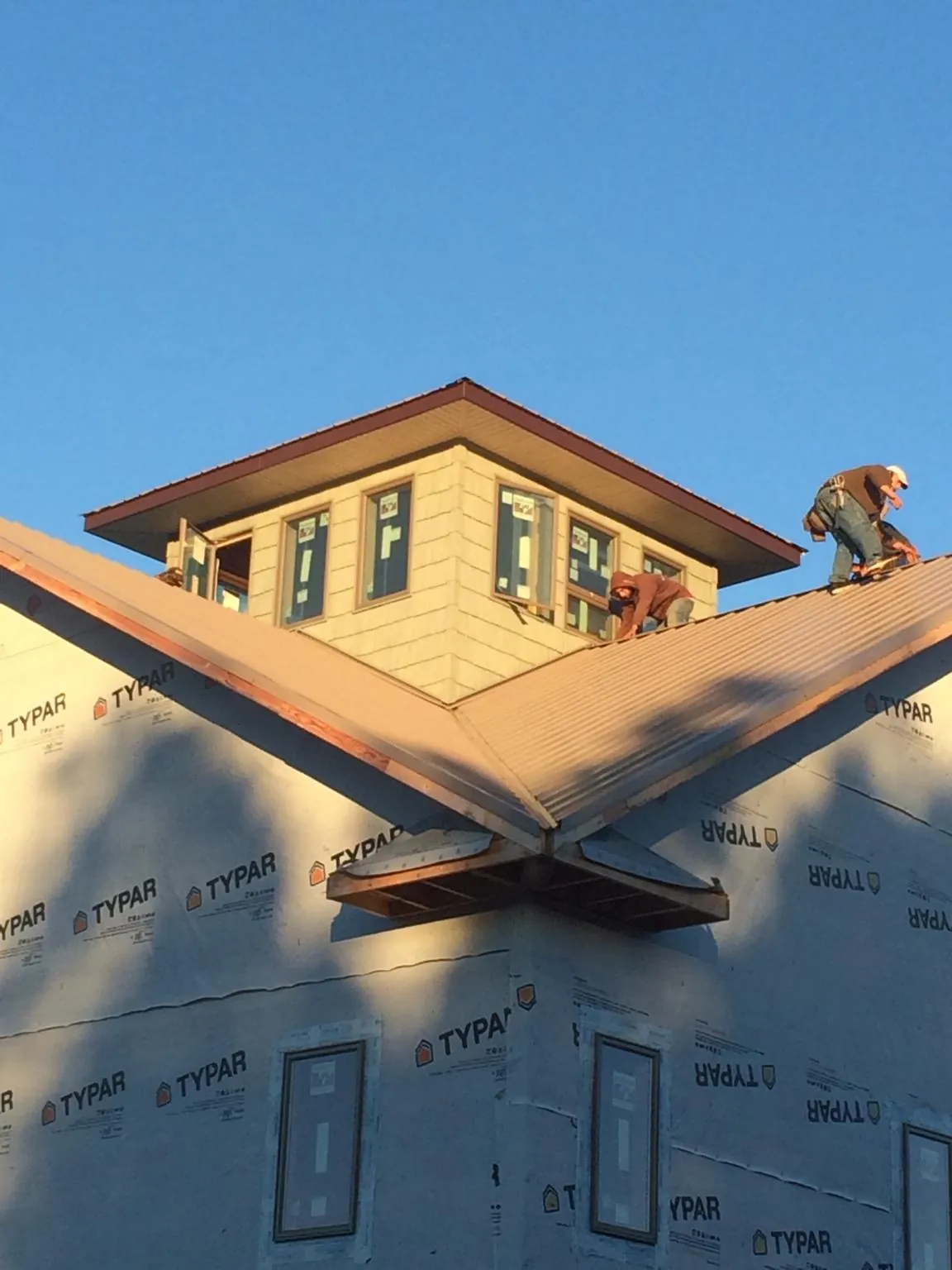 Roofers working around a rooftop cupola on a new metal roof at sunset — Roof Waterproofing in West Des Moines by Roofing Brothers